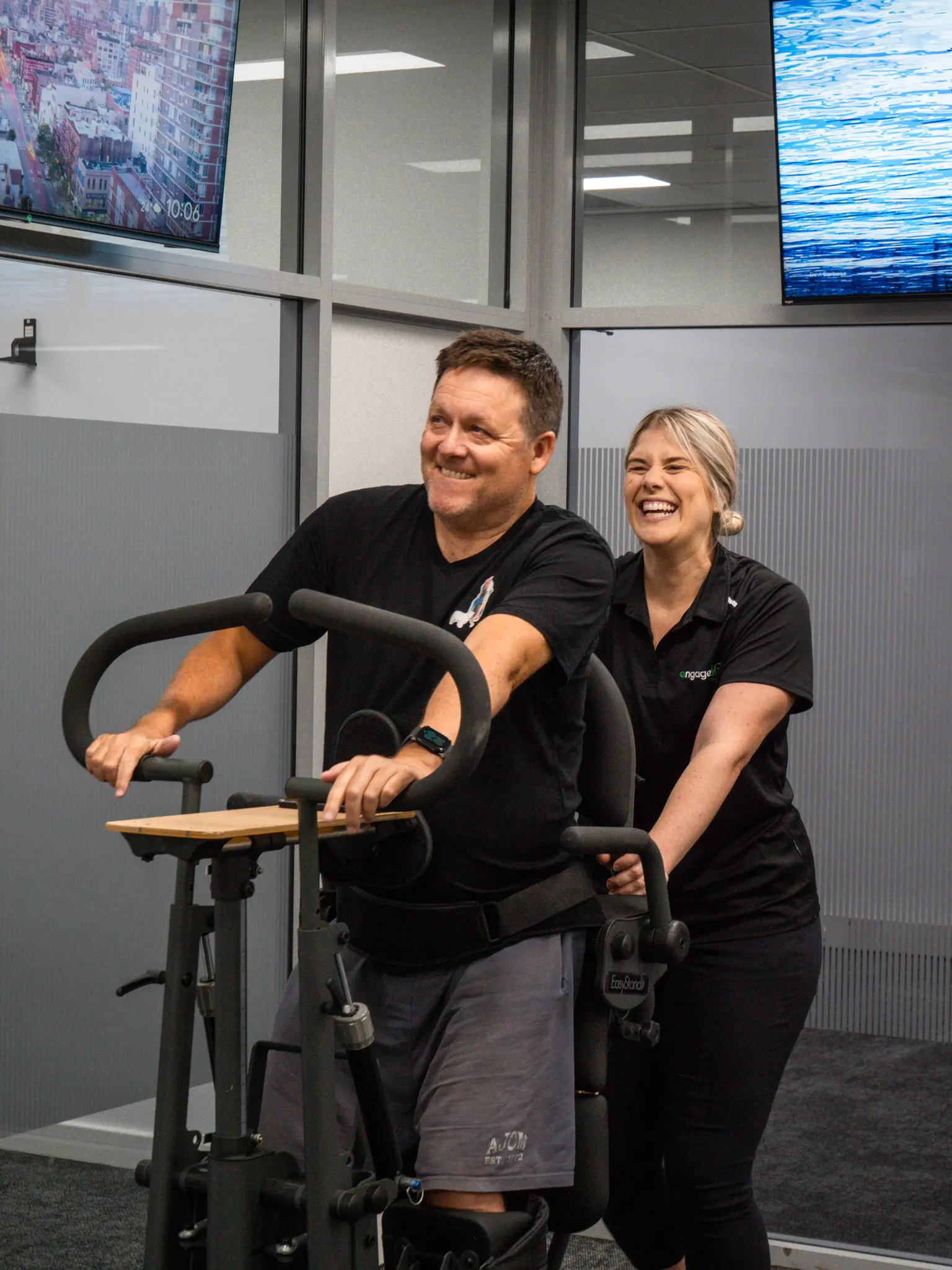 A client laughing with an Engage clinician while training in a supported standing frame