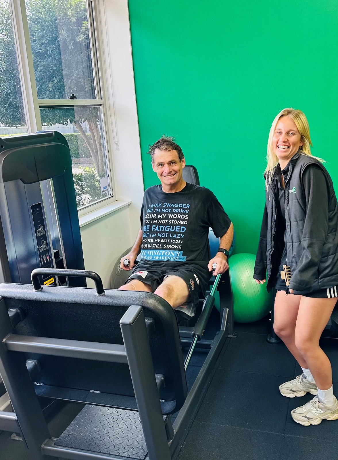A client and an Engage clinician smiling together beside the leg press in the studio