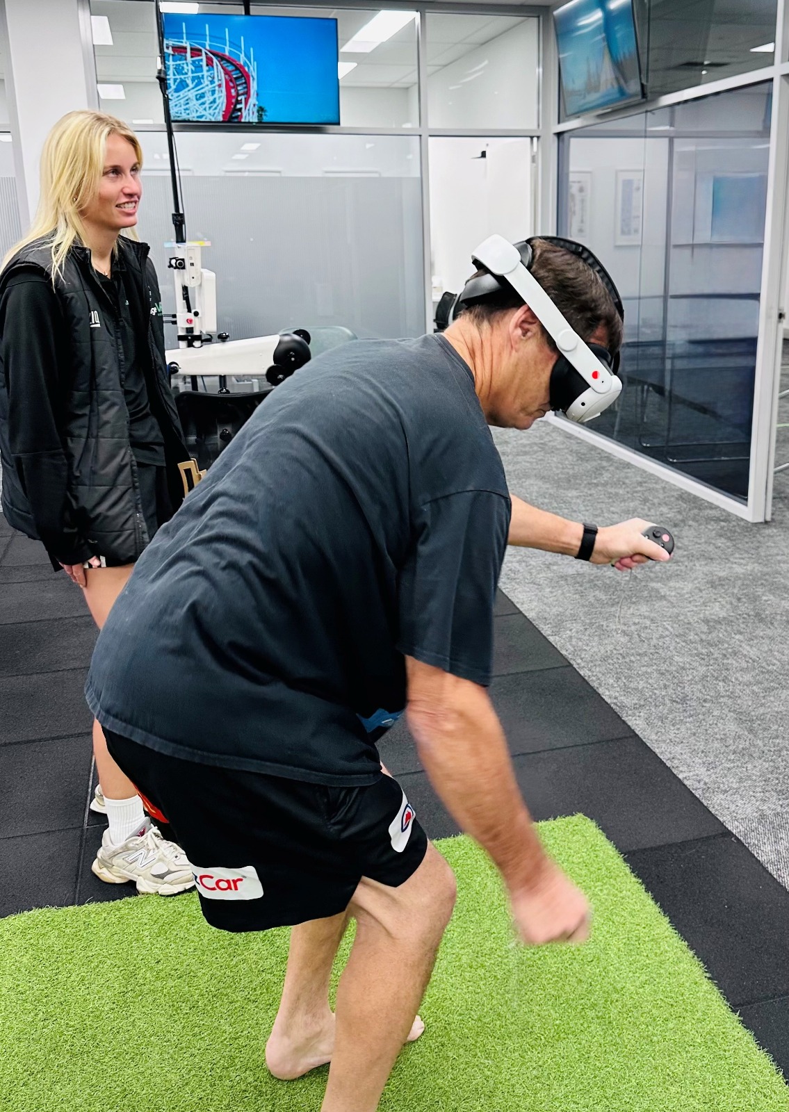A client in a VR headset working through a reaching and balance task on the studio turf, watched by an Engage clinician